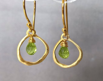 May include: Gold earrings with a delicate, irregular circle design and a single green gemstone hanging from each earring.