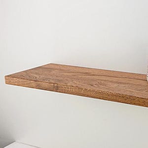 May include: A wooden shelf with a natural finish, featuring a small potted succulent and a decorative ceramic object. The shelf is mounted on a white wall.