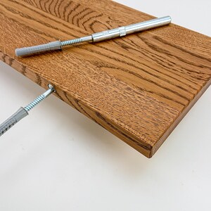 May include: A close-up of a wooden shelf with two gray plastic anchors and screws. The shelf is made of light brown wood with a natural grain pattern.