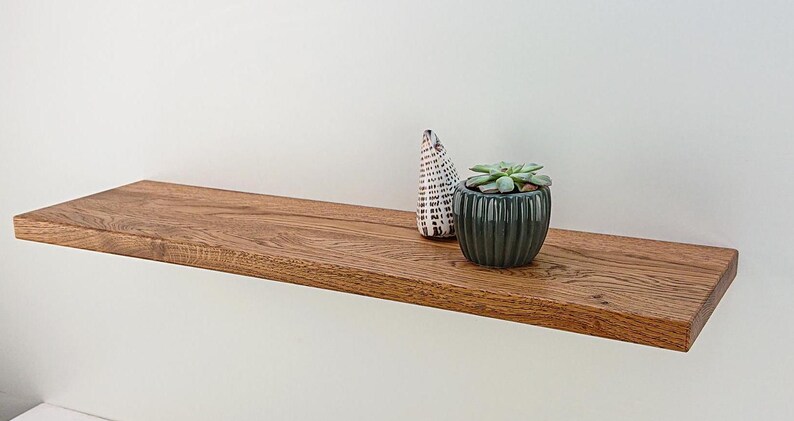 May include: A wooden shelf with a natural finish, featuring a small potted succulent and a decorative ceramic object. The shelf is mounted on a white wall.