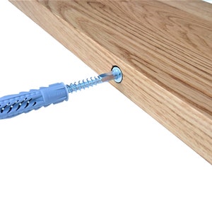 Pu&ograve; includere: Primo piano di un tassello da parete in plastica grigia con una vite argentata inserita al suo interno. La vite &egrave; parzialmente inserita in uno scaffale di legno.