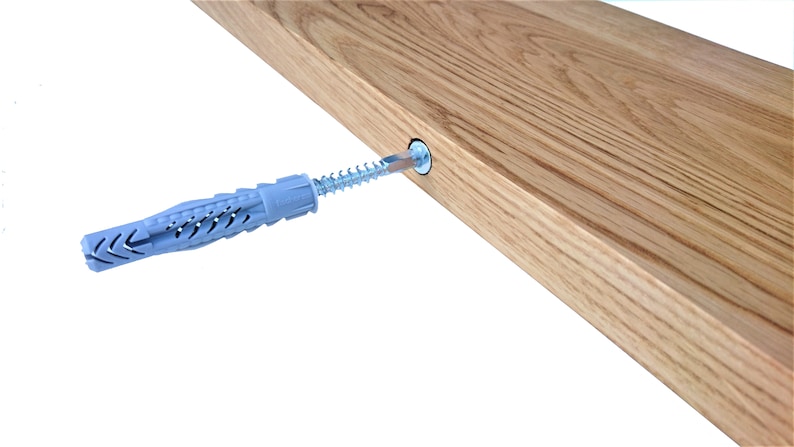 Pu&ograve; includere: Primo piano di un tassello da parete in plastica grigia con una vite argentata inserita al suo interno. La vite &egrave; parzialmente inserita in uno scaffale di legno.
