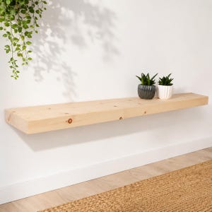 Könnte beinhalten: Ein schwebendes Regal aus hellem Holz an einer weißen Wand. Zwei kleine Topf-Sukkulenten stehen auf dem Regal. Das Regal hat eine sichtbare Holzmaserung. Auf dem Boden liegt ein gewebter Teppich.