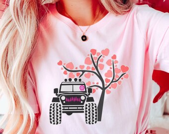 May include: Pink t-shirt featuring a black jeep graphic with a heart-shaped tree design. The word "PINK" is printed in the lower right corner. The shirt is a light pink color.