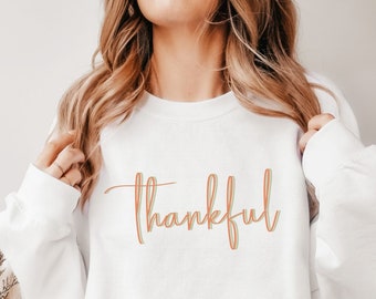 Może przedstawiać: Biała bluza z napisem "thankful" napisanym kolorowym, ozdobnym pismem.