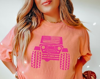 May include: Terracotta-colored t-shirt featuring a bright pink graphic of a Jeep with an American flag on the top. The shirt has short sleeves and a relaxed fit. The word "TERRACOTTA" is printed at the bottom of the image.