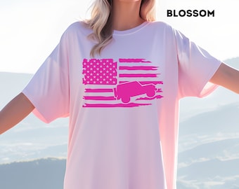 May include: A pink oversized t-shirt with a distressed American flag design featuring a pink silhouette of a jeep. The text "BLOSSOM" is in the top right corner of the image.