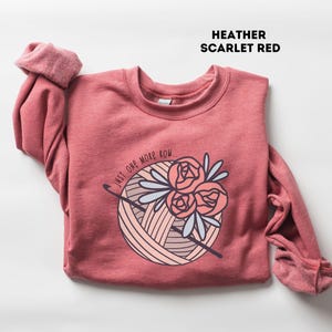 May include: Heather scarlet red sweatshirt with a graphic of a ball of yarn with flowers and the text "Just one more row".