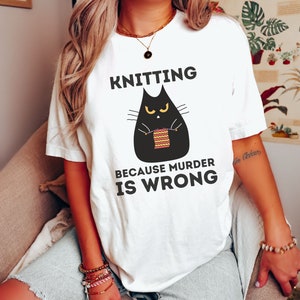 May include: White t-shirt with a black cat knitting a striped ball of yarn. The text on the shirt reads "Knitting because murder is wrong."