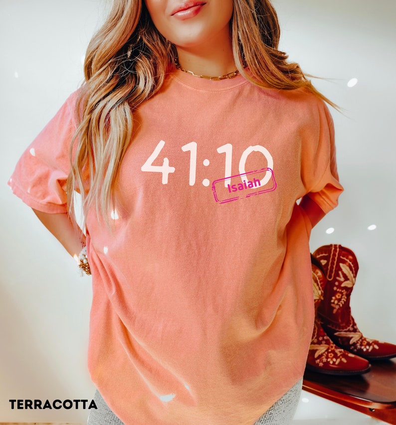 Puede incluir: Camiseta de color terracota con el texto "41:10 Isaiah" impreso en blanco.