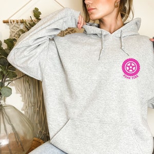 K&ouml;nnte beinhalten: Ein grauer Kapuzenpullover mit einem rosafarbenen Reifen-Motiv und dem Text "Pink Tire" auf der Vorderseite. Der Pullover ist mit "Sport Grey" gekennzeichnet.