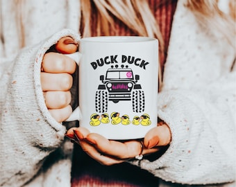 May include: White ceramic mug with a black and white graphic of a Jeep with the text "Duck Duck" above it. Five yellow rubber duckies with black sunglasses are lined up below the Jeep.