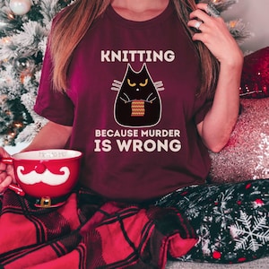 May include: A maroon t-shirt with a black cat knitting and the text "Knitting because murder is wrong".