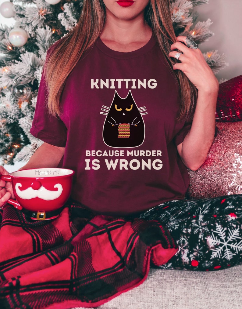 May include: A maroon t-shirt with a black cat knitting and the text "Knitting because murder is wrong".