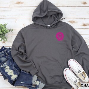 K&ouml;nnte beinhalten: Ein anthrazitfarbener Hoodie mit einem rosafarbenen Kreislogo, auf dem "Forever" steht. Der Hoodie hat eine Kapuze mit Kordelzug und eine K&auml;ngurutasche.