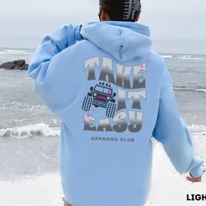 K&ouml;nnte beinhalten: Hellblauer Hoodie mit einem Grafikdruck eines Jeeps und dem Text "Take It Easy Offroad Club".