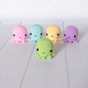 May include: Five crocheted octopus plushies in different pastel colors: pink, light blue, yellow, green, and purple. Each octopus has black eyes and a smiling expression.