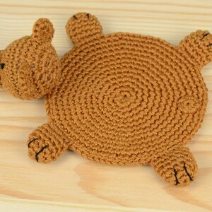 May include: A brown crocheted bear-shaped coaster with black eyes and nose.