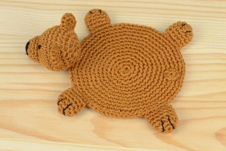 May include: A brown crocheted bear-shaped coaster with black eyes and nose.