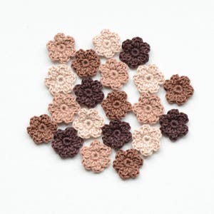 May include: A collection of crocheted flower embellishments in various shades of brown and beige. The flowers are all the same size and shape, and they are arranged in a random pattern.