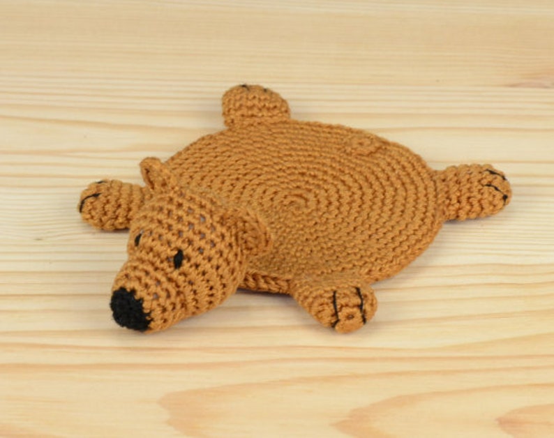 May include: A brown crocheted bear-shaped coaster with black eyes and a black nose.