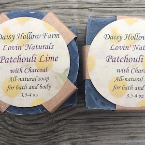 May include: Two bars of dark gray soap with a brown paper wrapper. The label on the soap reads "Daisy Hollow Farm Lovin' Naturals Patchouli Lime with Charcoal All-natural soap for bath and body 3.5-4 oz".