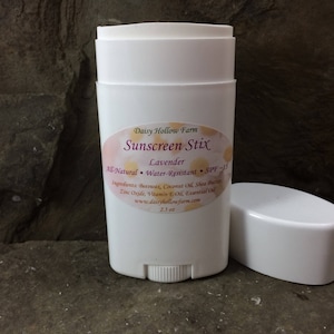 May include: White sunscreen stick with a label that reads "Daisy Hollow Farm Sunscreen Stix Lavender All-Natural Water-Resistant SPF-15 Ingredients: Beeswax, Coconut Oil, Shea Butter, Zinc Oxide, Vitamin E Oil, Essential Oil www.daisyhollowfarm.com 2.1 oz"