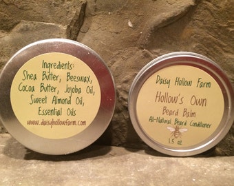 Può includere: Due barattoli di metallo, uno con un'etichetta che elenca gli ingredienti di un balsamo per barba, tra cui burro di karité, cera d'api, burro di cacao, olio di jojoba, olio di mandorle dolci e oli essenziali. L'altro barattolo ha un'etichetta che recita "Daisy Hollow Farm Hollow's Own Beard Balm All-Natural Beard Conditioner 1.5 oz."