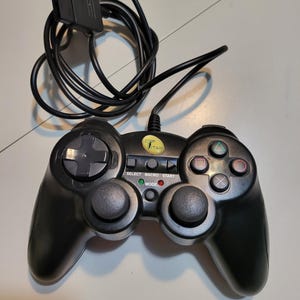 May include: Black Titan brand video game controller with a black cable and connector. The controller has a directional pad, buttons, and analog sticks. The controller has the words "SELECT", "MACRO", and "START" printed on it.