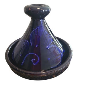 May include: A blue and black ceramic tagine with a decorative design. The tagine has a round base and a conical lid with a small opening at the top.