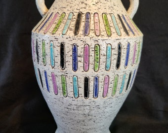 May include: White ceramic vase with a speckled finish and colorful geometric design. The vase has two handles and a rounded body.