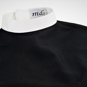 May include: A black clergy shirt with a white collar and a small white label with the text "md" on the collar.