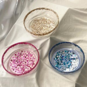 May include: A white ceramic mug with a black handle and the text "But First, Coffee" in a black, bold font. The mug is sitting on a wooden surface. The mug is approximately 4 inches tall.