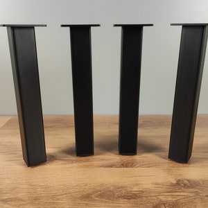 May include: Four black metal table legs with a square top. The legs are standing on a wooden surface.