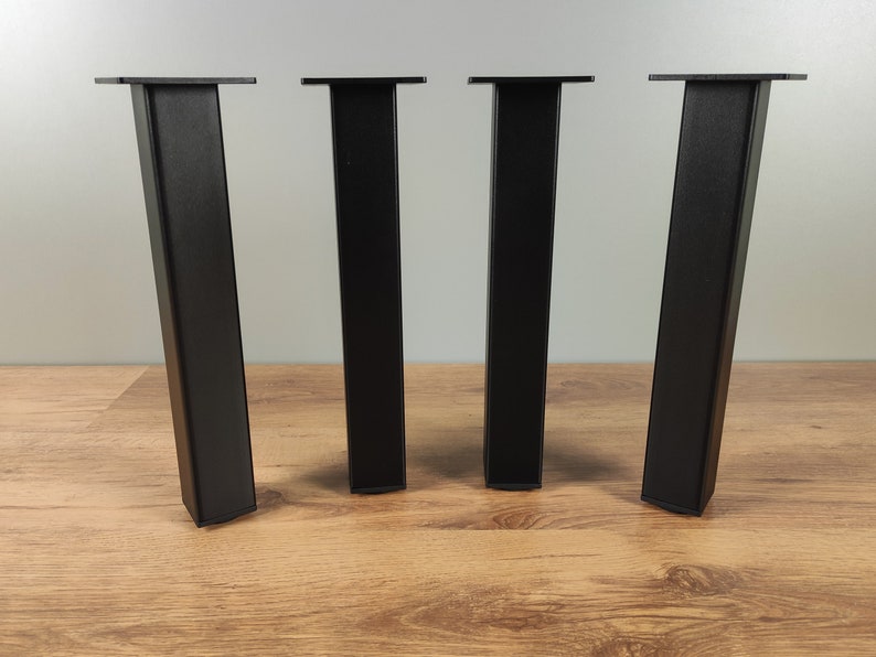 May include: Four black metal table legs with a square top. The legs are standing on a wooden surface.