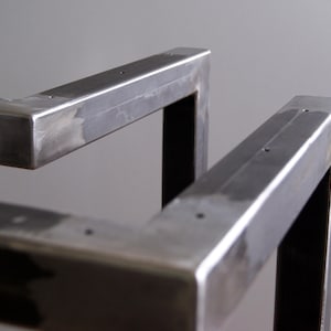 K&ouml;nnte beinhalten: Nahaufnahme eines Metalltischbeins mit geschwei&szlig;ter Konstruktion. Das Bein besteht aus quadratischen Rohren und hat eine geb&uuml;rstete Oberfl&auml;che.