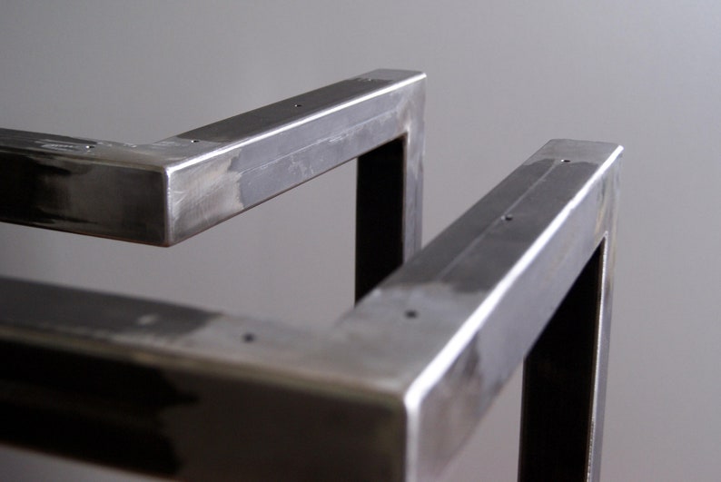 K&ouml;nnte beinhalten: Nahaufnahme eines Metalltischbeins mit geschwei&szlig;ter Konstruktion. Das Bein besteht aus quadratischen Rohren und hat eine geb&uuml;rstete Oberfl&auml;che.
