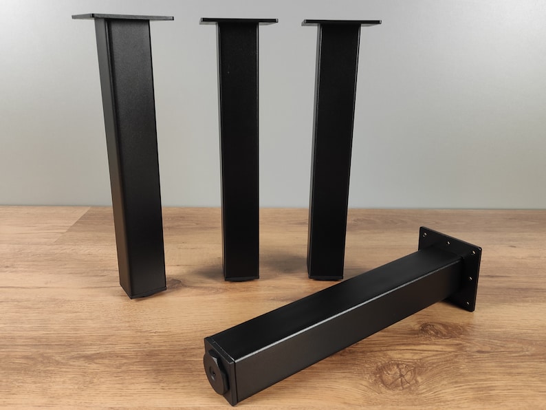 May include: Four black metal table legs with square tops. The legs are approximately 12 inches tall.