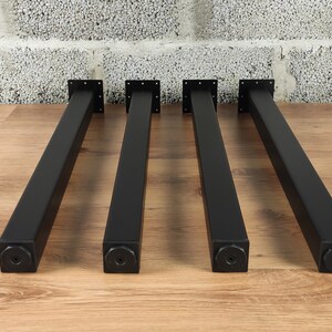 May include: Four black metal table legs with square bases. The legs are approximately 18 inches tall.