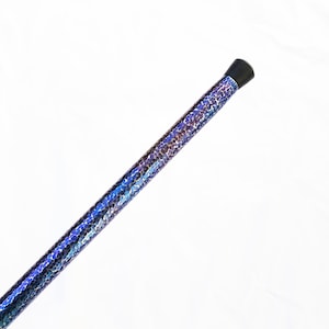 Op de afbeelding: Een lange, cilindrische staaf met een levendige, iriserende afwerking met een herhalend patroon van kleine, glinsterende blauwe, paarse en donker metallic schubben. Het uiteinde van de staaf is afgewerkt met een gladde, zwarte dop.