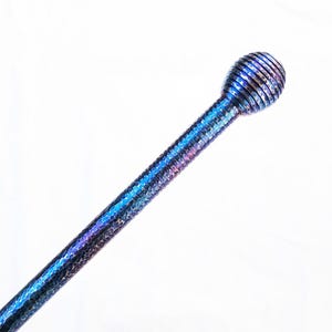 Op de afbeelding: Een lange, slanke metalen staaf met een getextureerd, gehamerd oppervlak met een iriserende blauwe en paarse afwerking. De staaf eindigt in een bolvormige, geribbelde knop aan de bovenkant, met dezelfde metallic uitstraling en kleurverloop.
