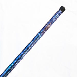 Op de afbeelding: Een lange, cilindrische wandelstok met een levendig, iriserend blauw en paars schubachtig patroon dat de gehele schacht bedekt. De bovenkant van de stok is afgewerkt met een gladde, effen zwarte dop, wat zorgt voor een strak contrast.