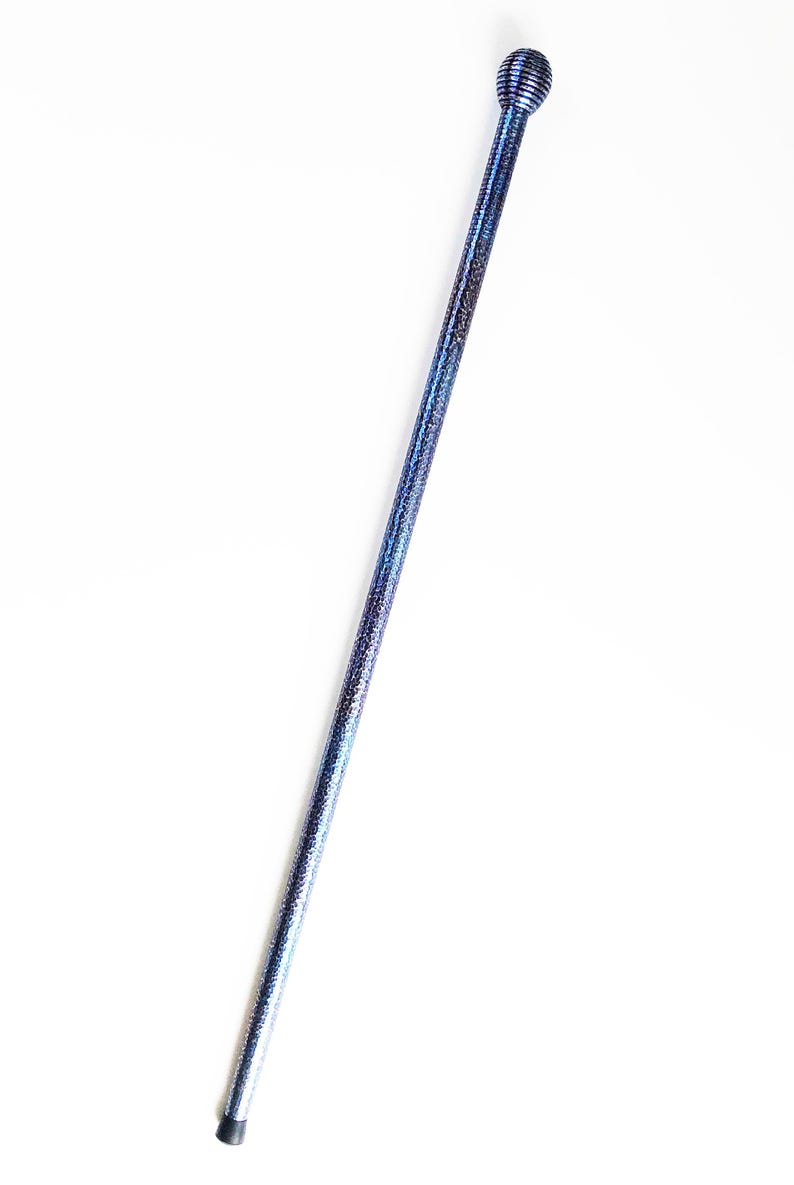 Op de afbeelding: Een lange, slanke wandelstok met een textuurrijke, glinsterende blauwe afwerking die naar onderen toe lichter wordt. Het handvat is een bolvormige, geribbelde knop en de onderkant is voorzien van een kleine, zwarte rubberen dop.