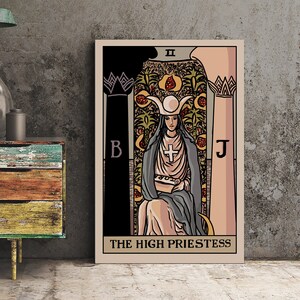 May include: A framed tarot card print of The High Priestess. The artwork features a woman in a gray robe and hat, holding a scroll. The background includes columns, floral patterns, and the letters B and J. The title is printed at the bottom.