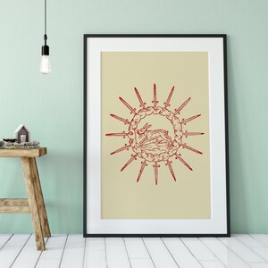 Può includere: Una stampa incorniciata con uno sfondo beige e un'illustrazione rossa di un cervo sdraiato circondato da un cerchio di spade.