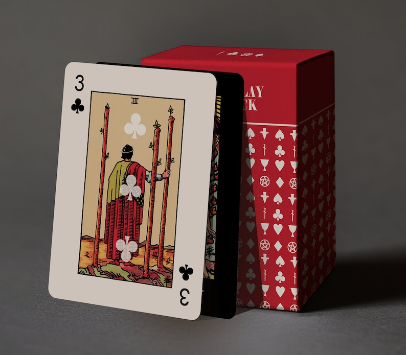 May include: A tarot card with the number 3 and three clubs is displayed in front of a red box. The card features an illustration of a person holding three staffs. The box is red with white symbols. The card is beige with black and red details.