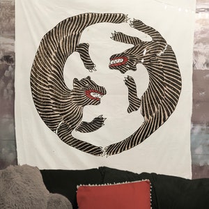 May include: A white tapestry with a black and white illustration of two stylized animals facing each other in a circle. The animals have red mouths and are drawn with a striped pattern.