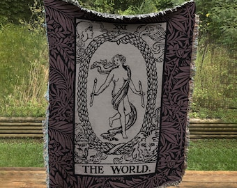 May include: A woven tapestry throw blanket featuring the The World tarot card. The card depicts a woman dancing within a wreath, with the number XXI and the words "THE WORLD" at the bottom.