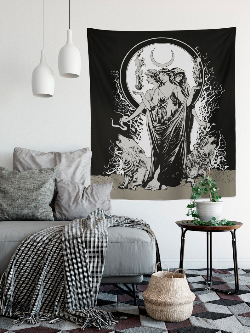 May include: Black and white tapestry featuring a triple goddess figure with a crescent moon above her head. She is surrounded by wolves and branches. The tapestry is hanging on a white wall in a living room setting.