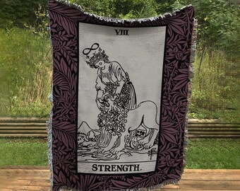 May include: A woven tapestry featuring the Strength tarot card. The card depicts a woman with a crown of infinity, gently holding the mouth of a lion. The card is framed by a purple floral border and the text "VIII STRENGTH" is printed at the bottom.